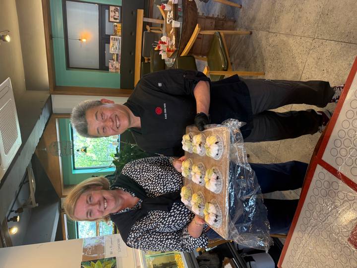 Two smiling participants proudly holding a tray of freshly made rice cakes in a workshop