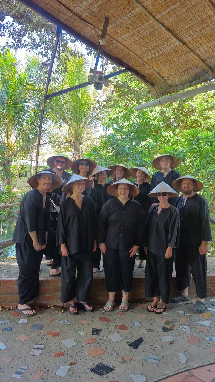 Tour group wearing Vietnamese conical hats poses together amidst lush greenery.