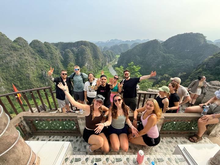 Excited travellers celebrate at a mountaintop viewpoint overlooking dramatic limestone karsts and a river.