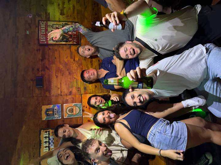 Nightlife scene of friends partying in a bar, holding beers and posing enthusiastically.