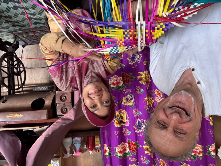 Traveller smiling with a local artisan holding colourful woven handicrafts inside a workshop.