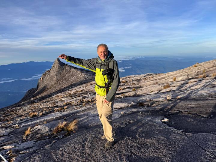 Hiker pointing toward a jagged granite peak on Mount Kinabalu’s barren summit plateau.
