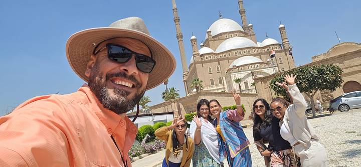 Selfie of smiling guide and group waving in front of the domes and minarets of the Mosque of Muhammad Ali.