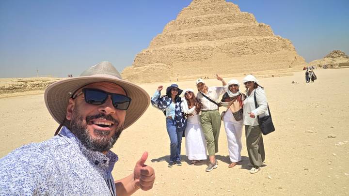 Tour group giving thumbs up before the Step Pyramid of Djoser at Saqqara on a sunny day.