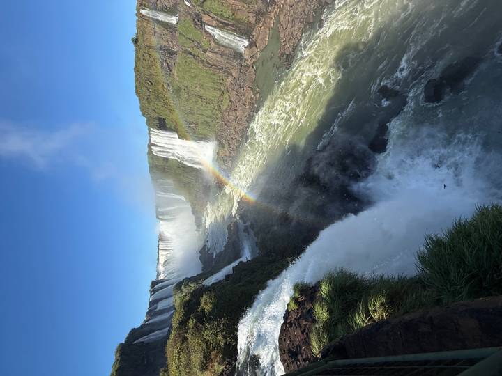 Spectacular Iguazu Falls cascade over lush cliffs with a vivid rainbow arcing through the mist.