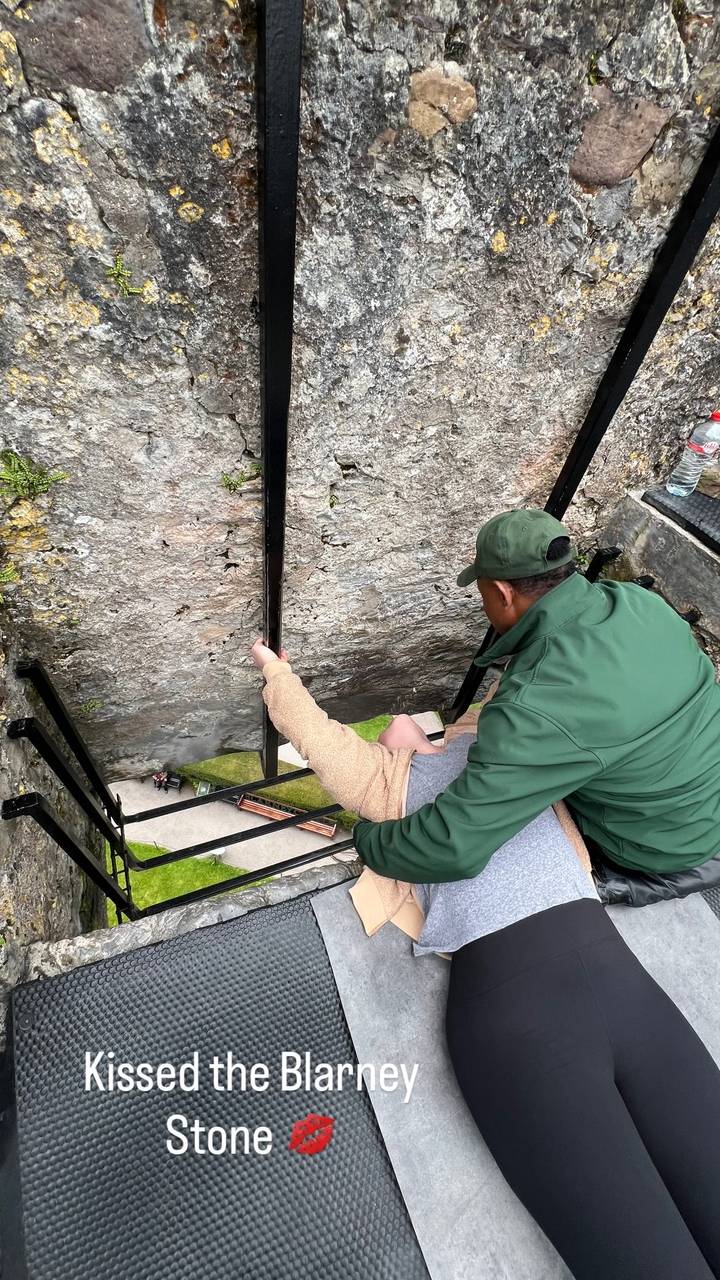 Guide steadies a visitor leaning backward to kiss the famous Blarney Stone within the castle parapet