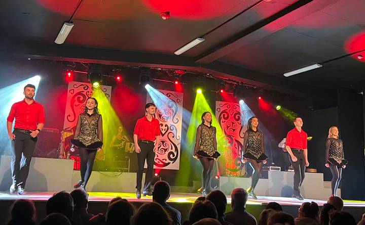 Lively Irish dance troupe performs on a brightly lit stage in coordinated red and black costumes