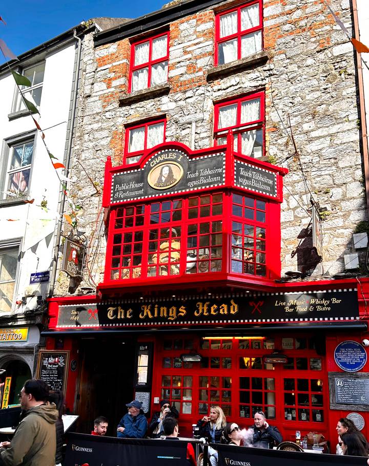 Bright red timber façade of The Kings Head pub stands out against a grey stone street in Galway