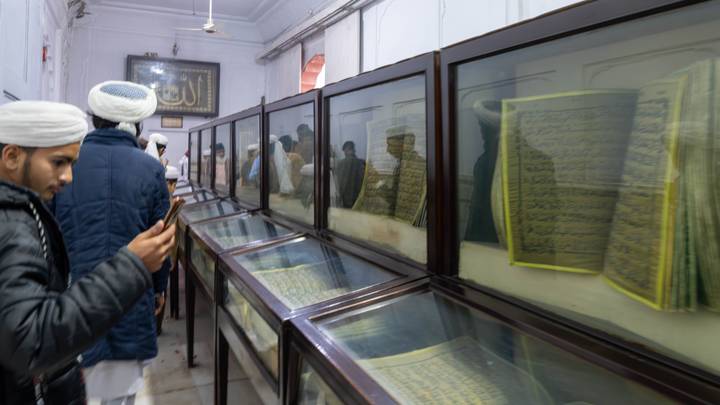 Visitors view glass cases displaying large pages of illuminated Qurans inside a religious museum hall.