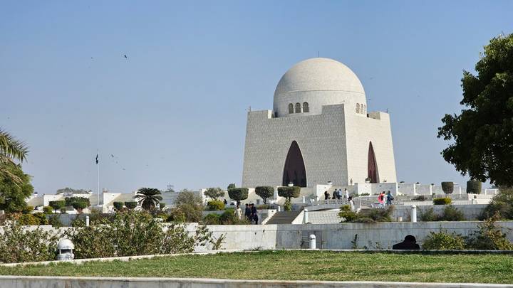 The white marble mausoleum of Mazar-e-Quaid rises against a clear blue sky with visitors in the surrounding gardens.