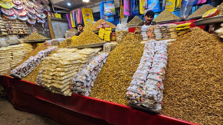 Heaped pyramids of nuts and sweets fill a vibrant market stall as two vendors serve customers.