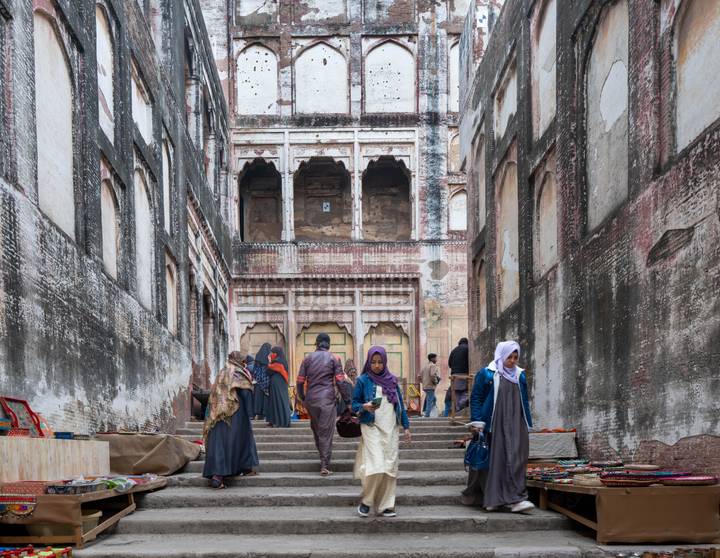 Visitors climb worn stone steps between tall historic walls toward an old Mughal-era gateway.