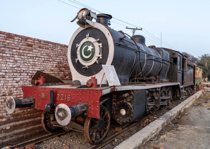 A preserved black steam locomotive bearing a crescent-star emblem is displayed beside a brick wall.