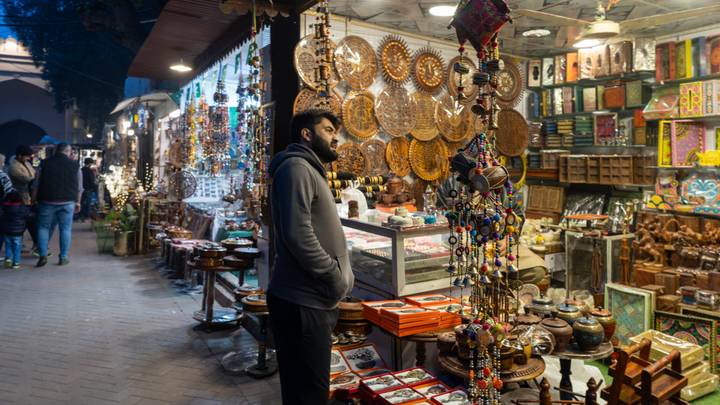 An evening bazaar alley lined with handicraft stalls and hanging ornaments as a man browses.
