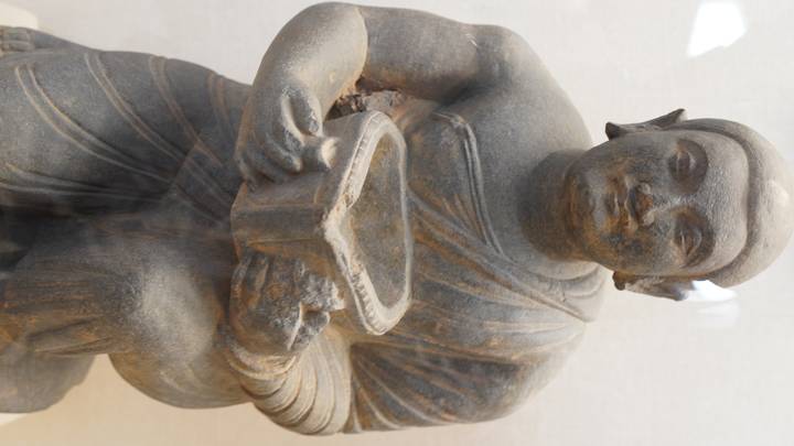 Stone sculpture of a kneeling ancient figure inside a museum display case.