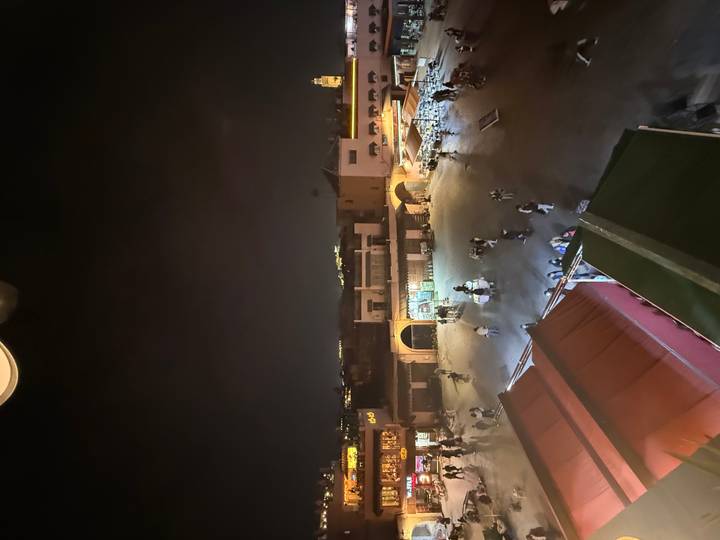 Nighttime overhead view of Jemaa el-Fnaa square with scattered shoppers and glowing shop lights.