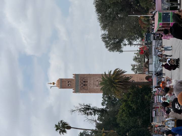 The Koutoubia Mosque minaret rises above palm trees and bustling crowds in Marrakesh.