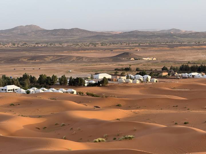 Wide view of white desert camps nestled among orange dunes and barren plains in the Sahara.