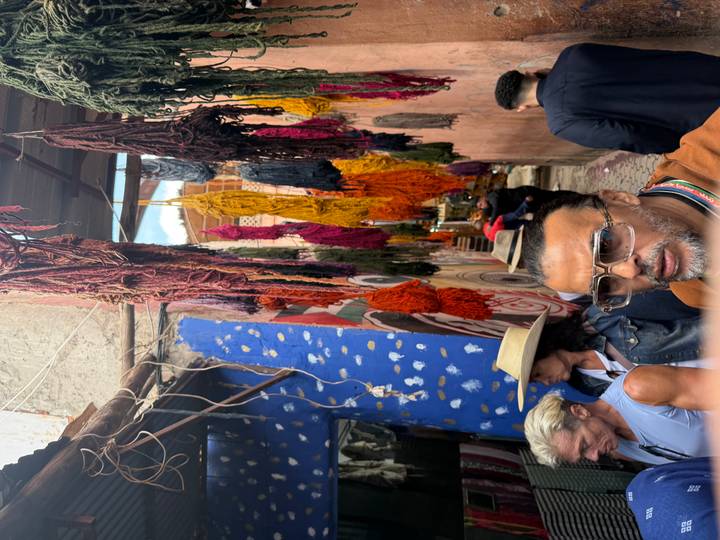 Colorful dyed yarns hang over a narrow alley in a Moroccan medina while tourists walk through and look around.