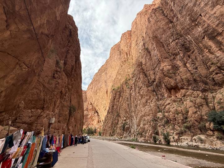 Towering ochre cliffs form a dramatic canyon with a winding road below and a partly cloudy sky above.