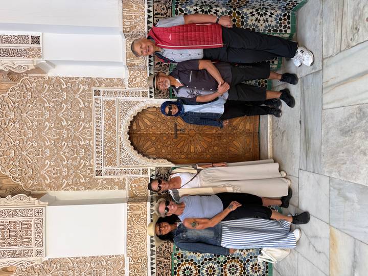 Tour group poses in front of an ornate carved doorway with intricate Moroccan tile and plaster work.