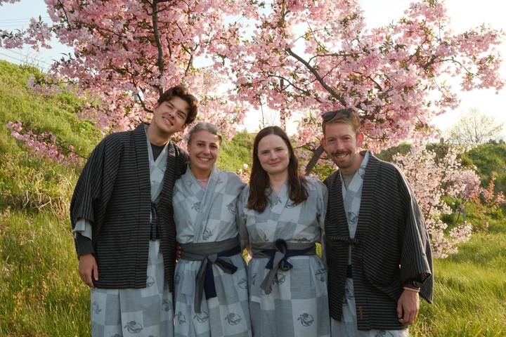 Four friends in yukata smiling beneath blooming cherry blossoms
