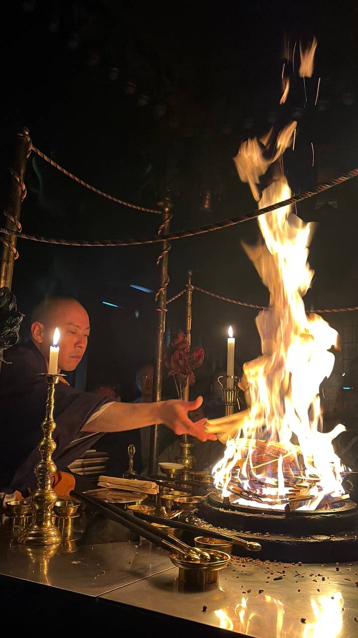 Monk performing fire ritual with tall flames and candles in dim temple