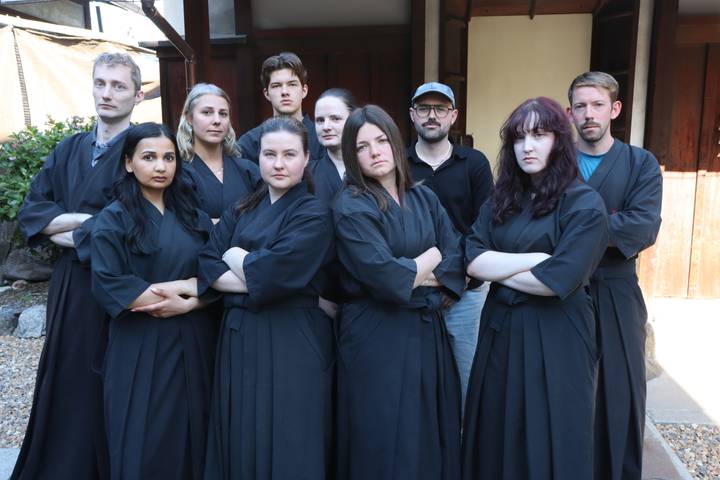 Group dressed in black martial arts robes posing with arms crossed outside dojo