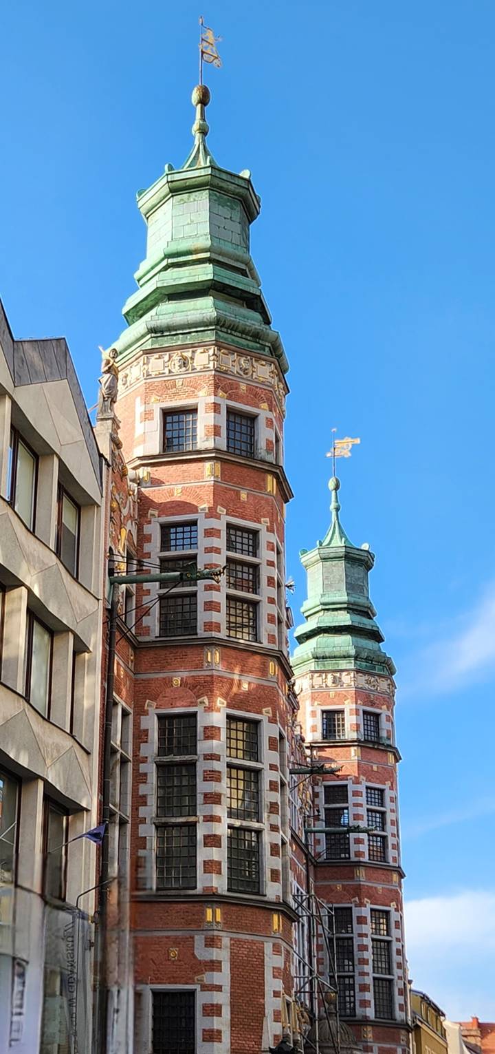 Close-up of a red-brick Renaissance tower and green copper spire against clear sky.