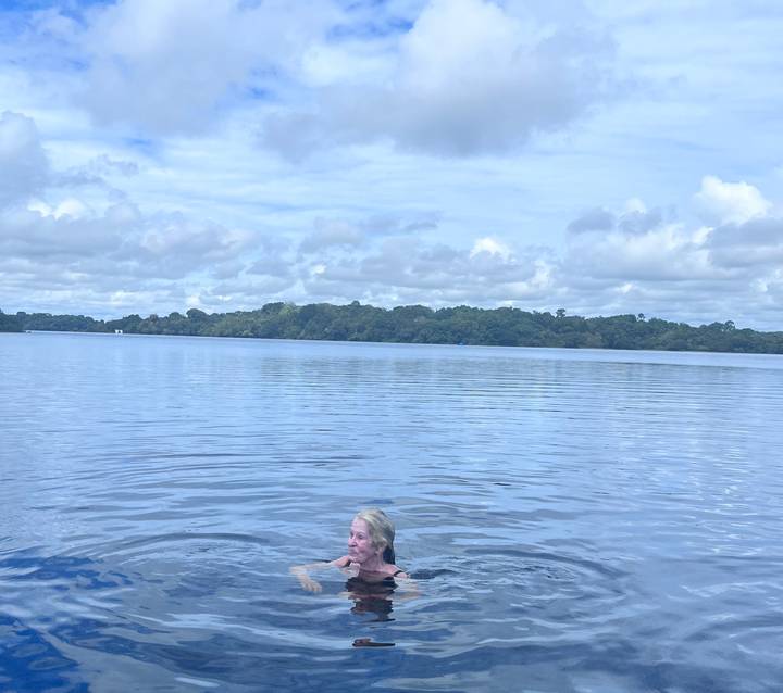 Woman swimming in a calm Amazon lagoon surrounded by lush forest under a partly cloudy sky