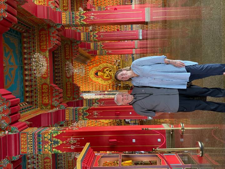 Couple standing inside a richly decorated Buddhist hall with golden Buddha statue