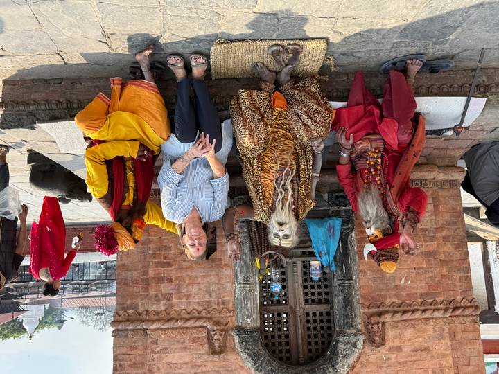 Visitor seated with three colorfully dressed sadhus posing outside a brick shrine at Pashupatinath