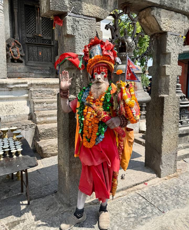 Brightly adorned sadhu with orange garlands raising his hand in blessing at Pashupatinath
