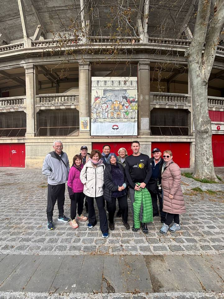 Smiling tour group posing in front of Pamplona bullring facade with cartoon banner.