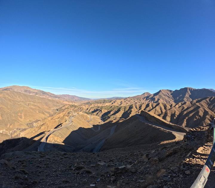 Sweeping view across rugged Atlas Mountains with winding road carving through valleys.
