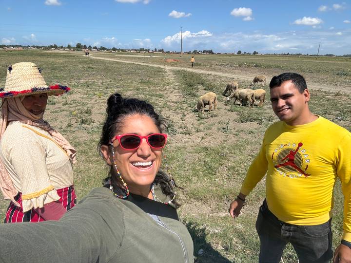 Travellers pose with local woman and grazing sheep on an open grassy plain.