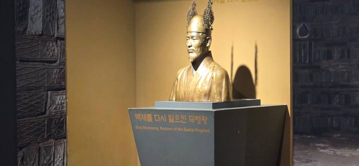Bronze bust of King Muryeong displayed on a pedestal in a dimly lit exhibit room.