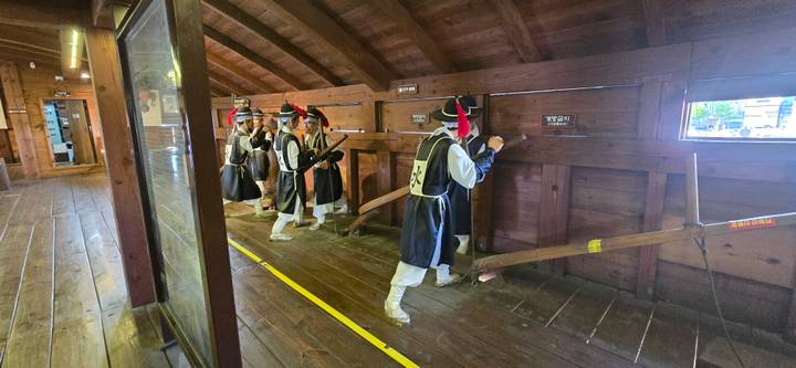 Costumed guards in traditional Korean clothing practising musket drill inside a wooden fortress corridor