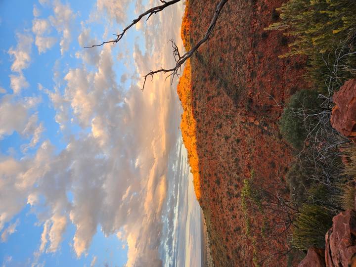 Red outback hills glowing in warm evening light beneath a dramatic cloud-dappled sky.