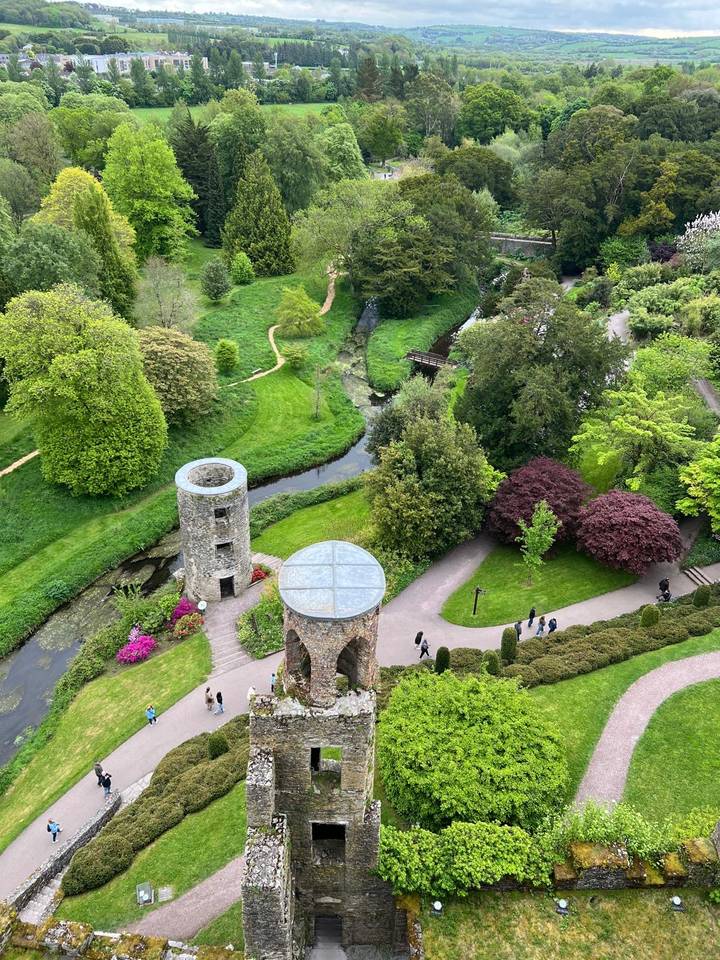 Birds-eye view of lush castle gardens with towers, winding paths, streams and tiny visitors below.