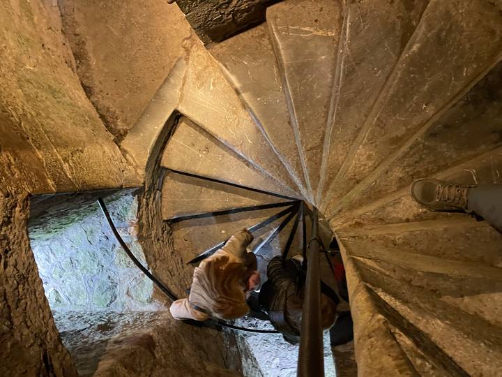 Looking down a narrow, worn stone spiral staircase inside a historic tower.