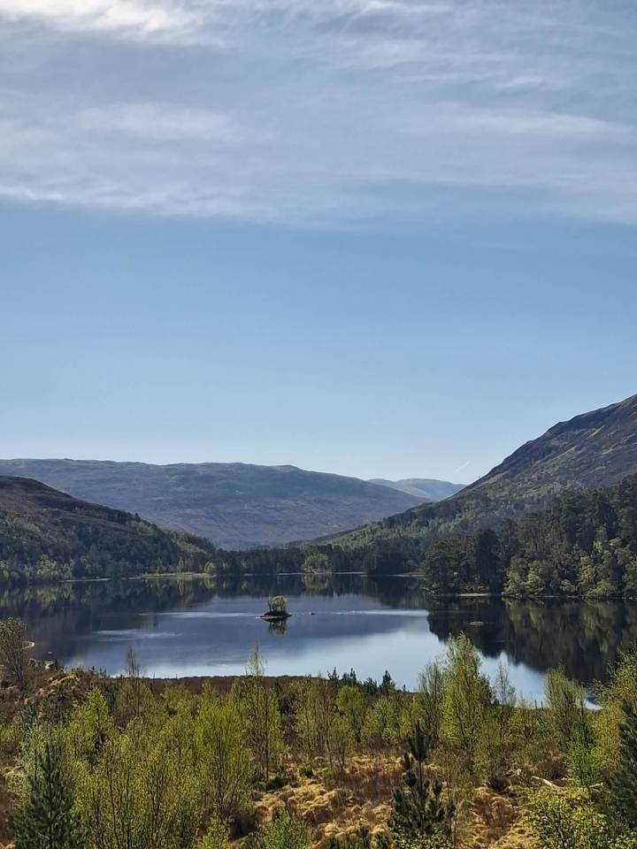 Serene Scottish loch reflecting forested hills beneath a clear blue sky