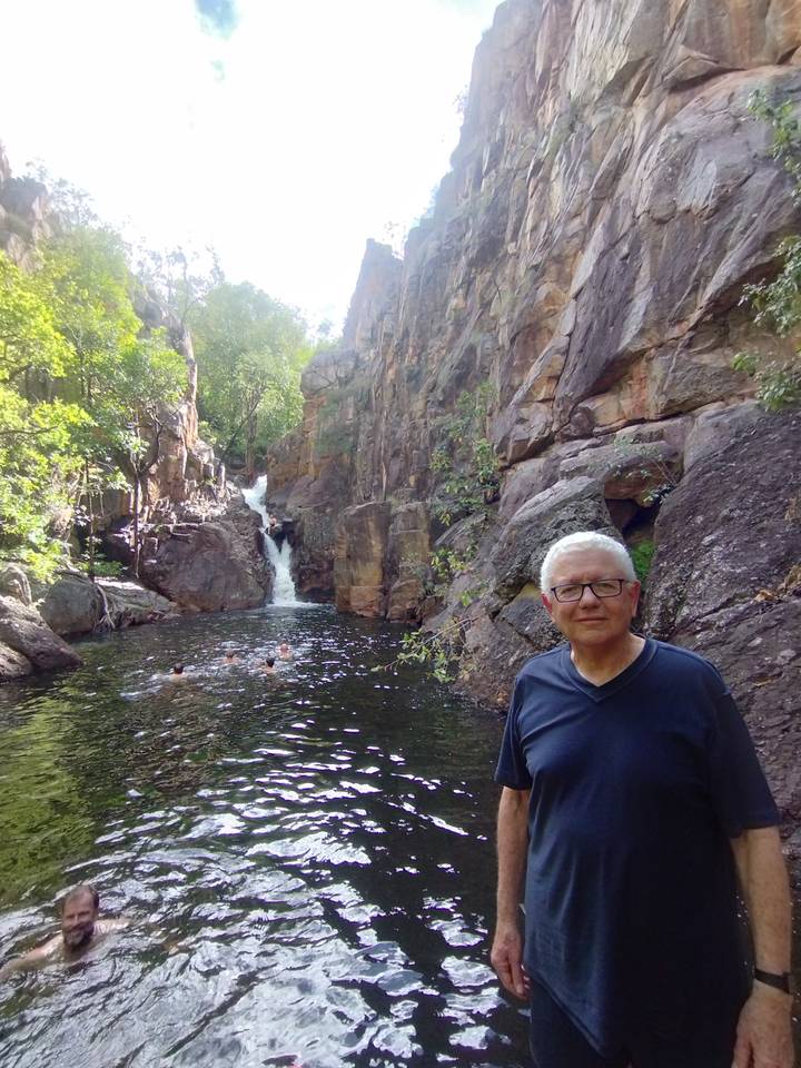 Visitor stands near a plunge pool and small waterfall while swimmers enjoy the water amid rugged cliffs