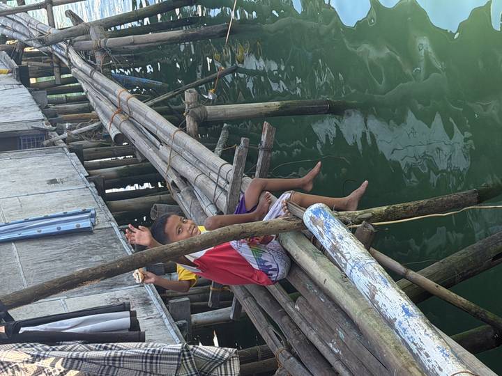 Smiling local boys waving from bamboo walkways over emerald coastal water