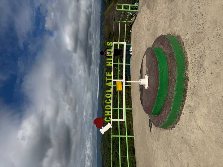 Viewpoint platform with 'Chocolate Hills' sign overlooking rolling green mounds