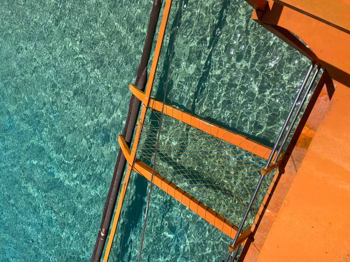 Close detail of a boat’s wooden ladder and netting over crystal-clear turquoise water.