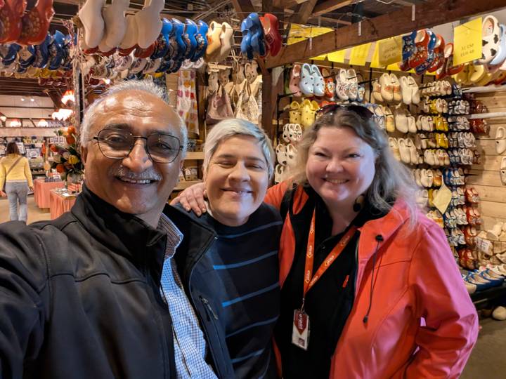 Three travellers smile inside a souvenir shop displaying rows of traditional wooden clogs and other goods.