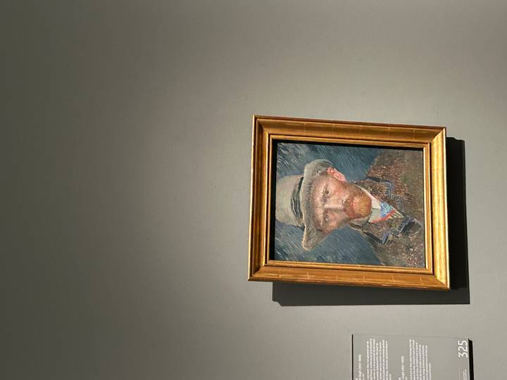 Framed self-portrait painting by Vincent van Gogh displayed on a grey museum wall.