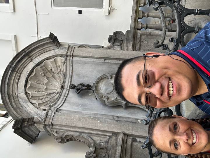 Selfie of travellers smiling in front of the famous Manneken Pis fountain in Brussels.