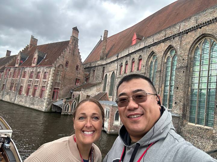 Couple posing beside a medieval brick hospital complex along a canal in overcast weather.
